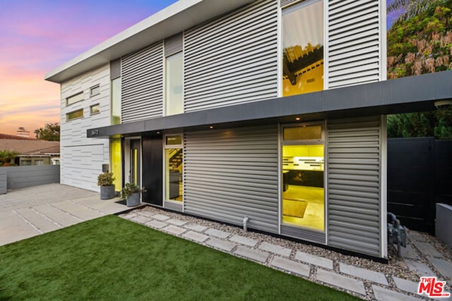 back house at dusk with a patio area and a lawn