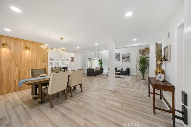 dining area featuring light hardwood / wood-style floors, wooden walls, and a chandelier