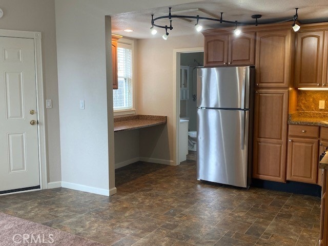 kitchen featuring dark stone countertops, tasteful backsplash, stainless steel refrigerator, and a textured ceiling