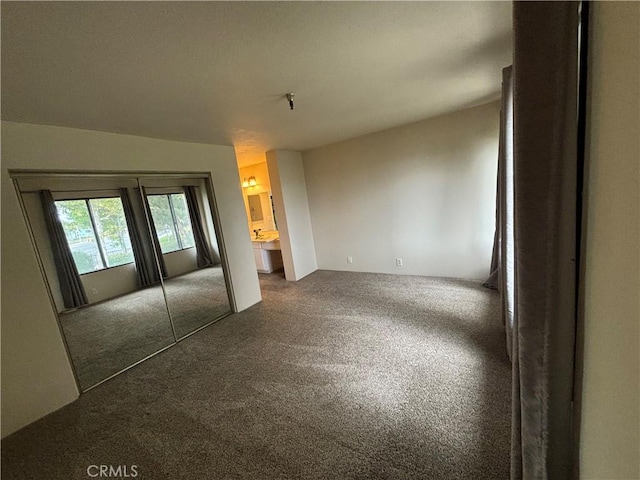 unfurnished bedroom featuring ensuite bathroom, a closet, and dark carpet