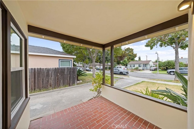 view of patio featuring covered porch, fence, and a residential view