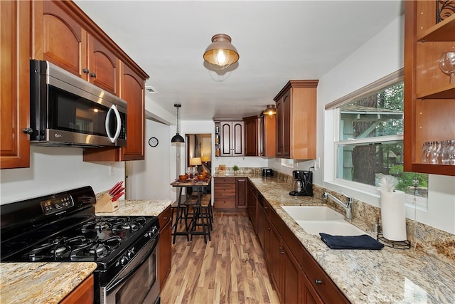 kitchen with light stone countertops, sink, light wood-type flooring, hanging light fixtures, and black gas range