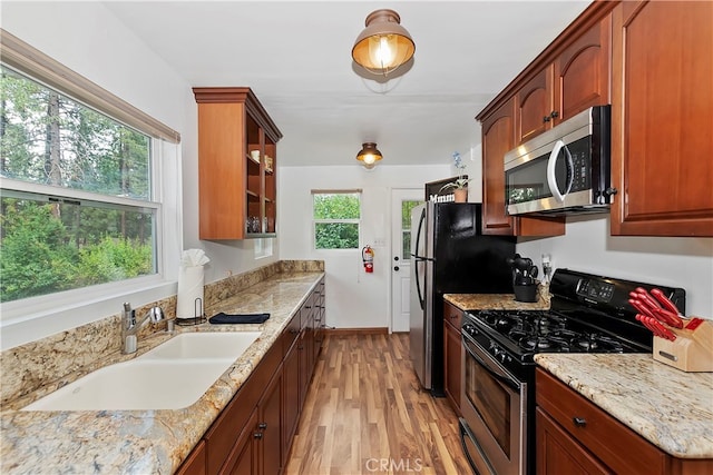 kitchen with light stone counters, sink, appliances with stainless steel finishes, and light hardwood / wood-style flooring