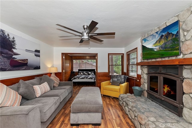 living room featuring wooden walls, hardwood / wood-style floors, a textured ceiling, a fireplace, and ceiling fan