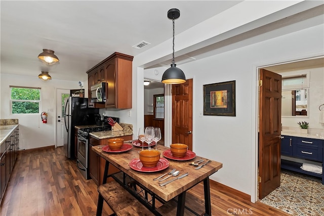 kitchen with dark wood-type flooring, stainless steel appliances, light stone countertops, and decorative light fixtures