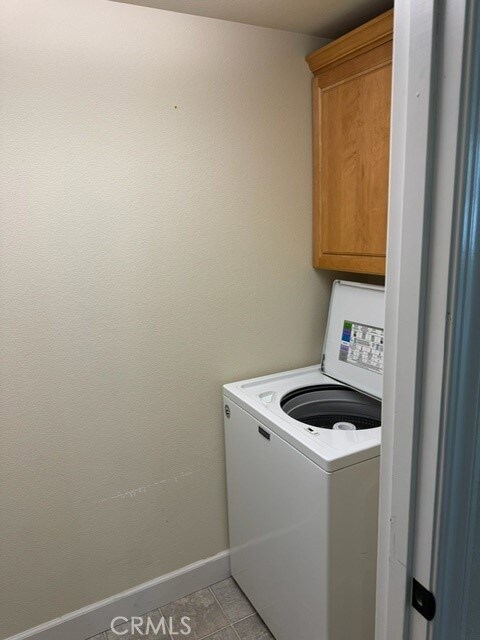 clothes washing area with washer / clothes dryer, light tile patterned flooring, and cabinets