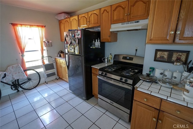 kitchen featuring tile counters, stainless steel range with gas cooktop, light tile patterned flooring, and black fridge