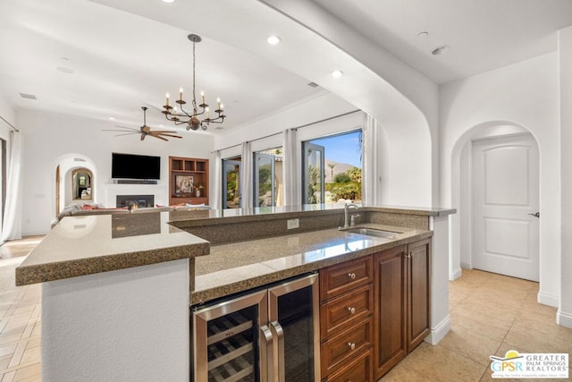 kitchen with sink, an island with sink, light stone counters, decorative light fixtures, and wine cooler