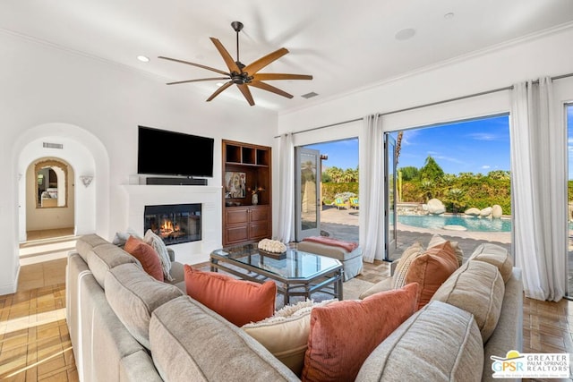 living room with ornamental molding, built in shelves, light parquet flooring, and ceiling fan