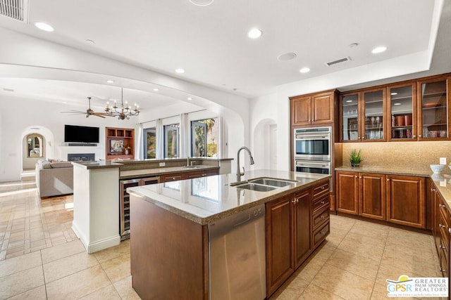 kitchen with decorative backsplash, appliances with stainless steel finishes, a kitchen island with sink, light tile patterned flooring, and sink