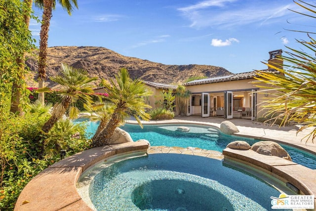 view of swimming pool featuring an in ground hot tub, a mountain view, a patio area, and french doors