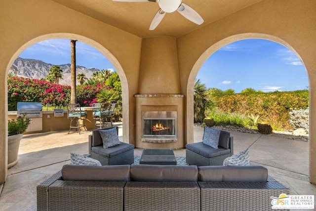 view of patio featuring area for grilling, exterior kitchen, ceiling fan, a mountain view, and an outdoor living space with a fireplace