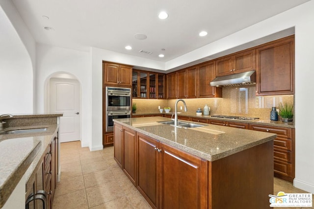 kitchen featuring a kitchen island with sink, sink, light stone countertops, and stainless steel appliances