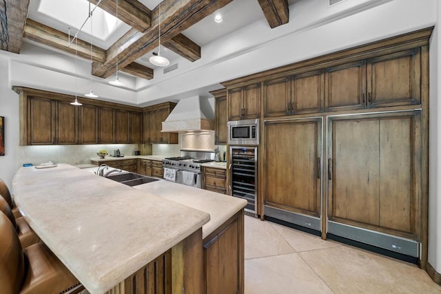 kitchen with coffered ceiling, a breakfast bar area, hanging light fixtures, custom exhaust hood, and appliances with stainless steel finishes