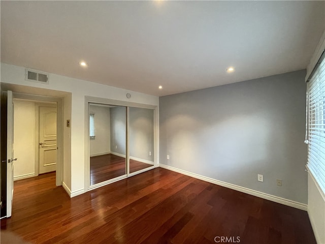 unfurnished bedroom with a closet, hardwood / wood-style flooring, and multiple windows