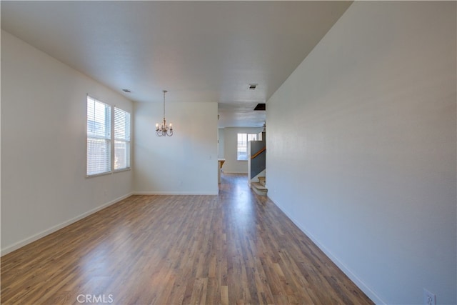 empty room featuring dark wood-type flooring, a notable chandelier, and a healthy amount of sunlight