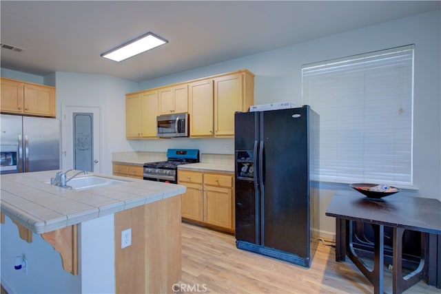 kitchen with light brown cabinets, appliances with stainless steel finishes, light hardwood / wood-style flooring, tile counters, and sink