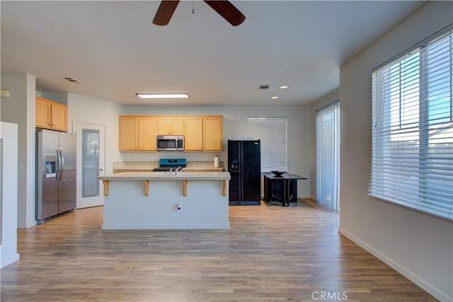 kitchen featuring ceiling fan, an island with sink, a kitchen bar, light wood-type flooring, and stainless steel appliances