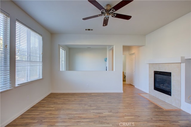 unfurnished living room with a tiled fireplace, light wood-type flooring, and ceiling fan