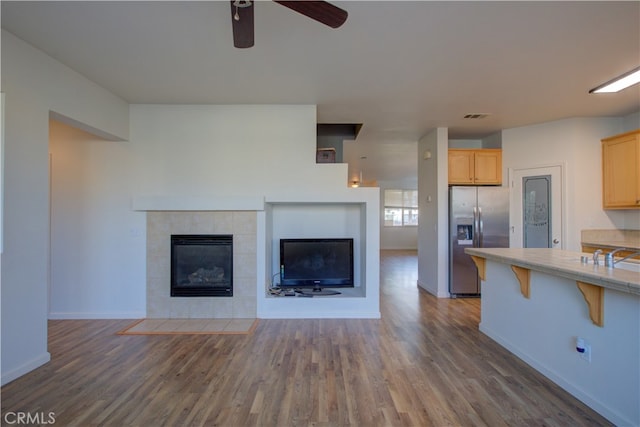 unfurnished living room with ceiling fan, a tile fireplace, and dark hardwood / wood-style floors