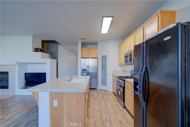 kitchen featuring tile countertops, stainless steel appliances, light brown cabinetry, and light hardwood / wood-style floors