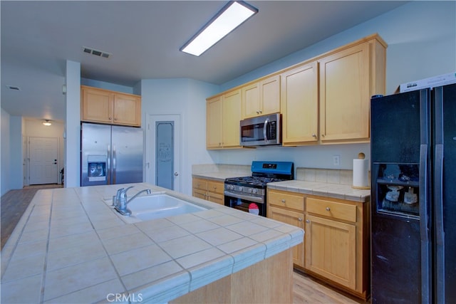 kitchen featuring tile countertops, sink, appliances with stainless steel finishes, and light brown cabinets