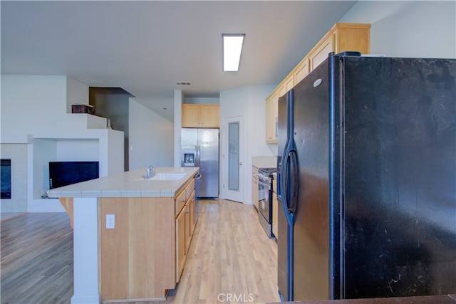 kitchen with appliances with stainless steel finishes, sink, light hardwood / wood-style floors, light brown cabinets, and a center island with sink