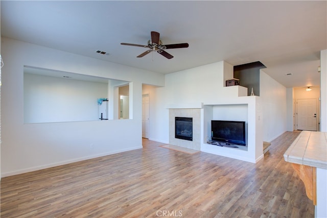 unfurnished living room with a tile fireplace, light wood-type flooring, and ceiling fan