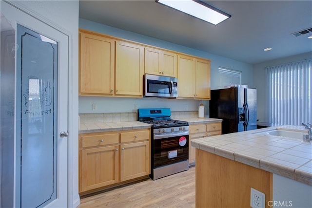 kitchen featuring light brown cabinets, stainless steel appliances, and tile counters