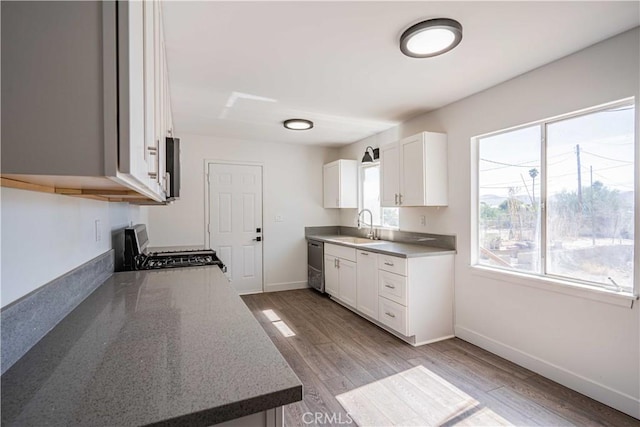 kitchen featuring white cabinets, sink, dark stone countertops, light wood-type flooring, and appliances with stainless steel finishes