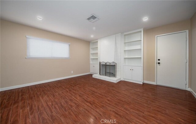 unfurnished living room featuring dark wood-type flooring and a brick fireplace