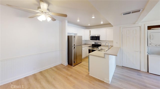 kitchen with light wood-type flooring, kitchen peninsula, white cabinetry, stainless steel appliances, and stacked washing maching and dryer