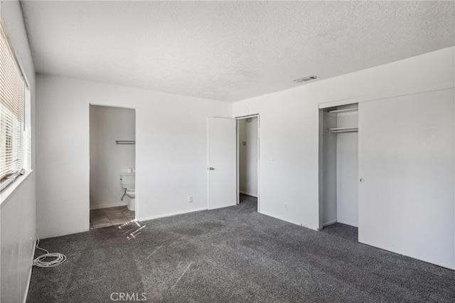 unfurnished bedroom with a closet, a textured ceiling, connected bathroom, and dark colored carpet