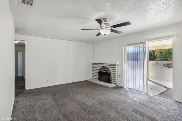 unfurnished living room with ceiling fan, a textured ceiling, a brick fireplace, and dark colored carpet