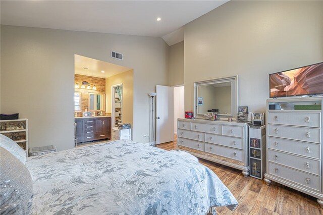 bedroom featuring wood-type flooring, high vaulted ceiling, and ensuite bath