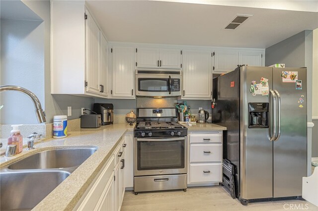 kitchen featuring appliances with stainless steel finishes, white cabinetry, sink, and light wood-type flooring