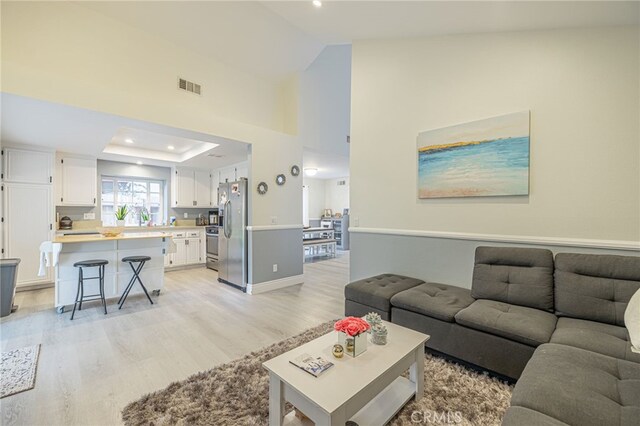 living room featuring light hardwood / wood-style floors, high vaulted ceiling, and a tray ceiling