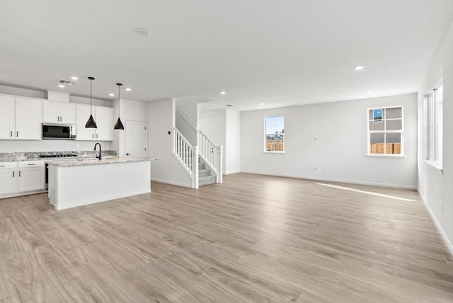 kitchen featuring hanging light fixtures, white cabinets, appliances with stainless steel finishes, and a center island with sink