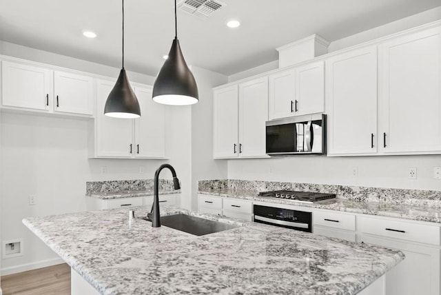 kitchen with pendant lighting, sink, appliances with stainless steel finishes, an island with sink, and white cabinets