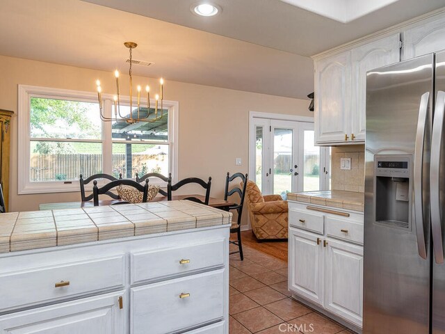 kitchen featuring white cabinetry, hanging light fixtures, tile counters, and stainless steel fridge