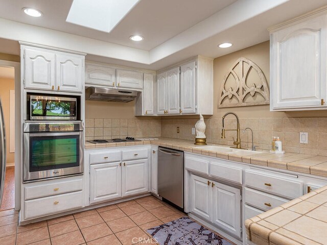 kitchen featuring white cabinets, light tile patterned floors, appliances with stainless steel finishes, tile countertops, and sink