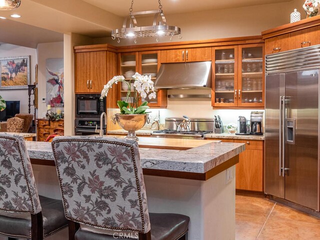 kitchen featuring a kitchen island, appliances with stainless steel finishes, light tile patterned floors, range hood, and decorative light fixtures