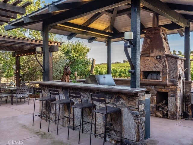 view of patio / terrace with a gazebo, an outdoor stone fireplace, a bar, and a pergola