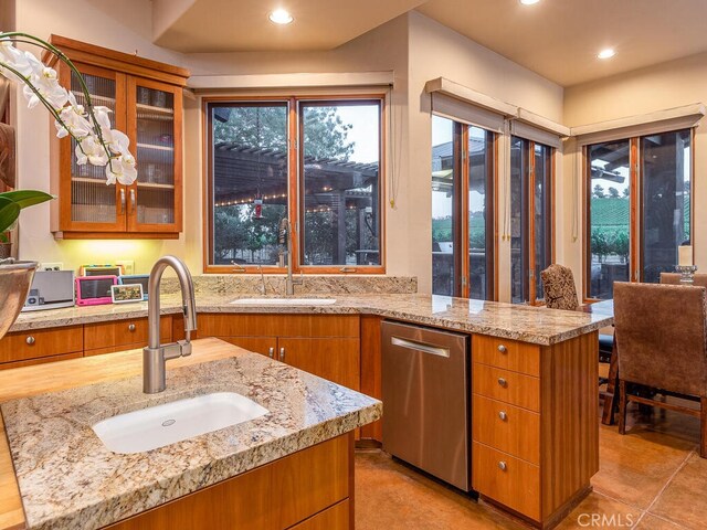 kitchen featuring light stone countertops, sink, stainless steel dishwasher, and a kitchen island