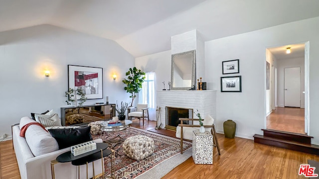 living room with wood-type flooring, vaulted ceiling, and a fireplace