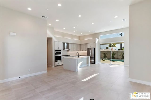 kitchen featuring wall chimney range hood, appliances with stainless steel finishes, sink, and a center island with sink