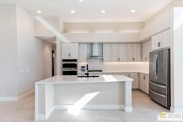 kitchen featuring appliances with stainless steel finishes, sink, light tile patterned flooring, wall chimney exhaust hood, and a kitchen island with sink