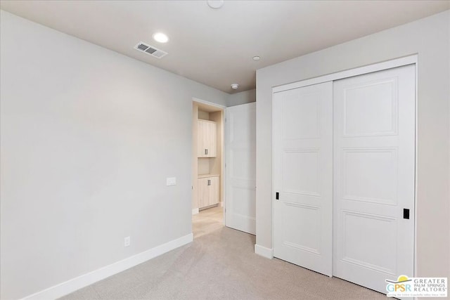 unfurnished bedroom with light colored carpet and a closet