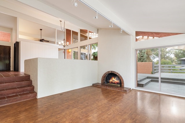 living room with lofted ceiling with beams, ceiling fan with notable chandelier, rail lighting, a brick fireplace, and dark hardwood / wood-style flooring