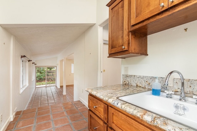 kitchen featuring sink, vaulted ceiling, light stone countertops, a textured ceiling, and light tile patterned flooring